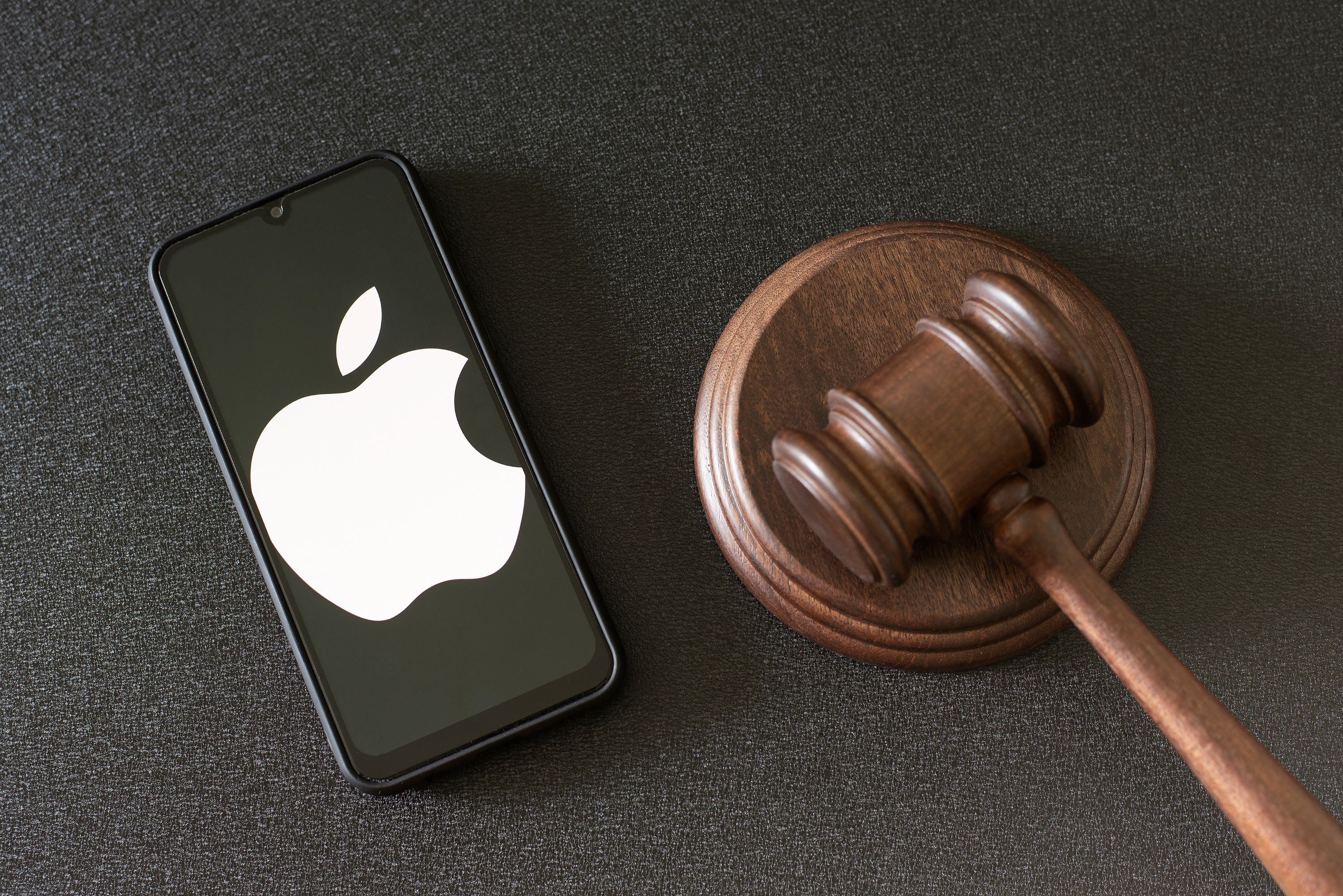 A smartphone displaying the apple logo sits next to a gavel on a flat surface.
