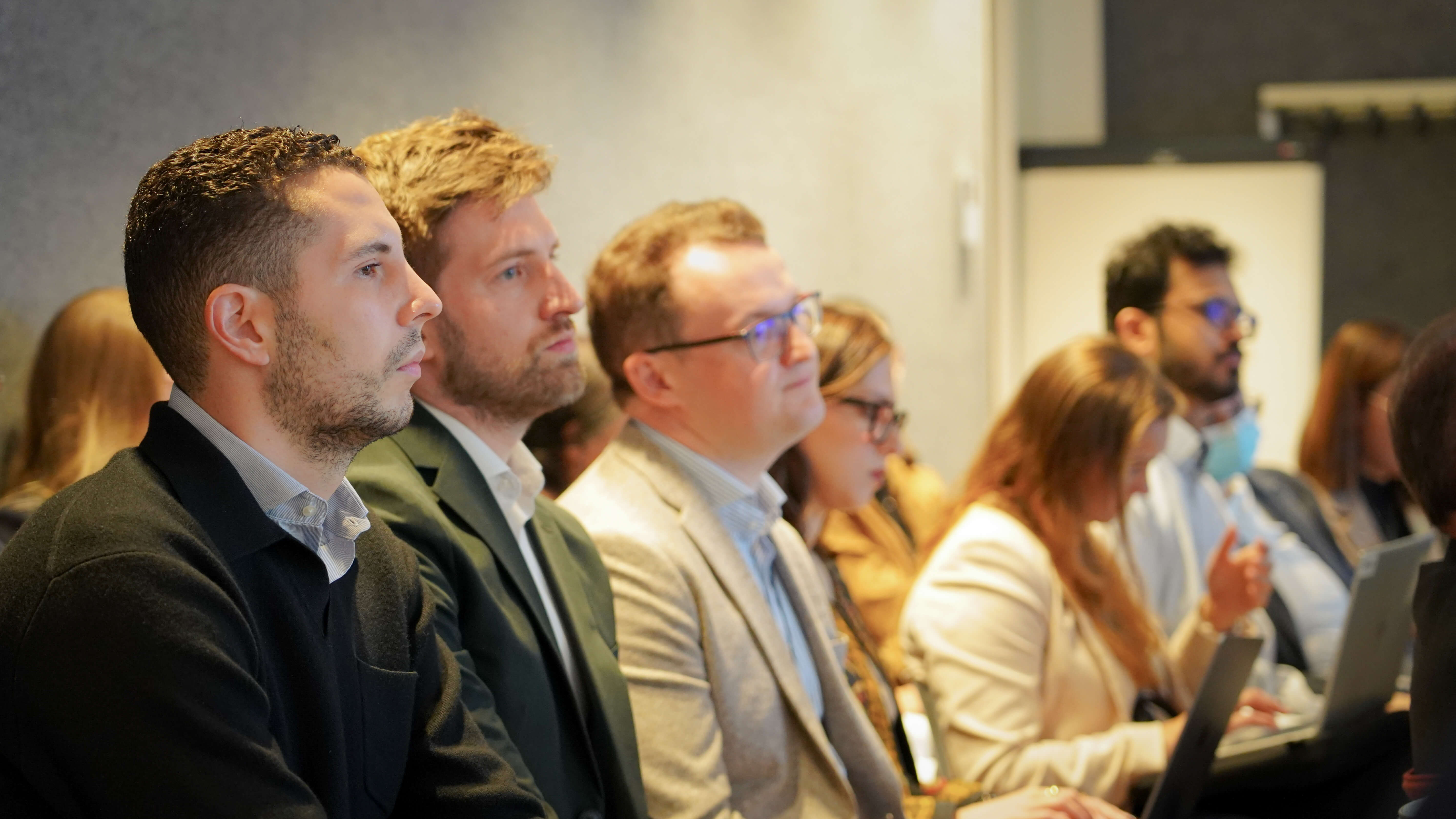 a crowd of people in business wear watches a conference presentation