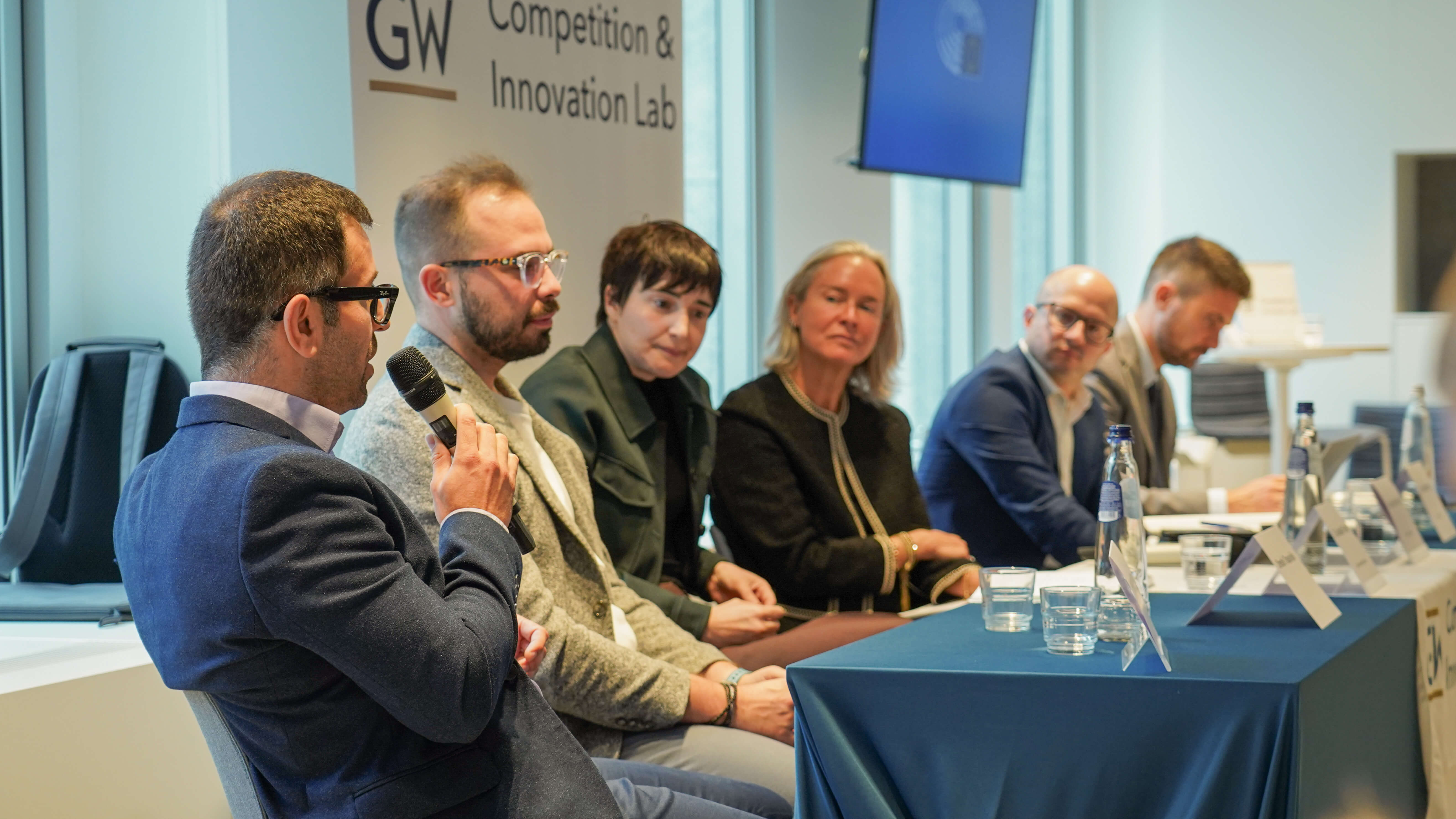 4 men and 2 women giving a conference presentation on a panel