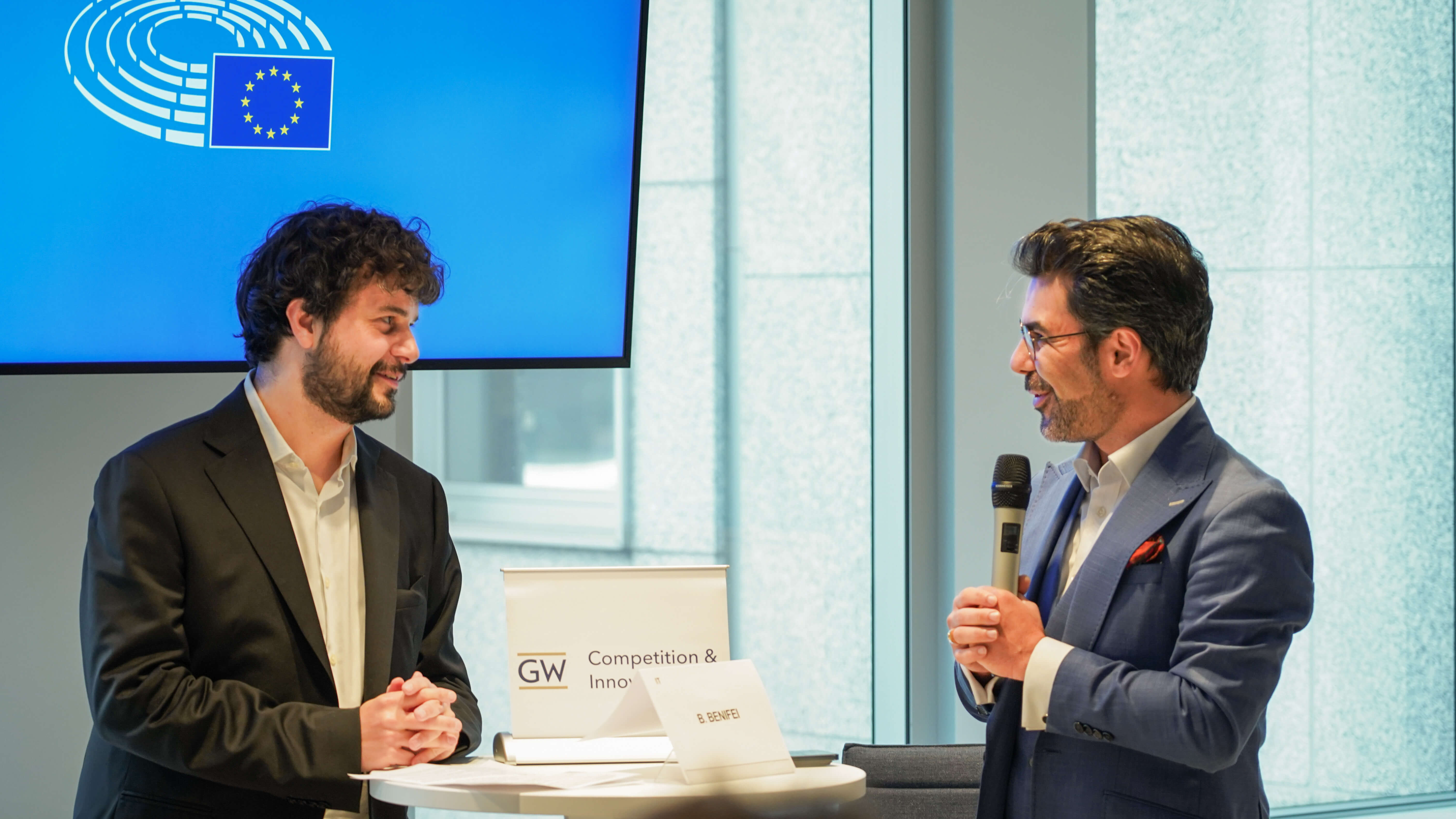 two men in suits having a discussion during a conference presentation