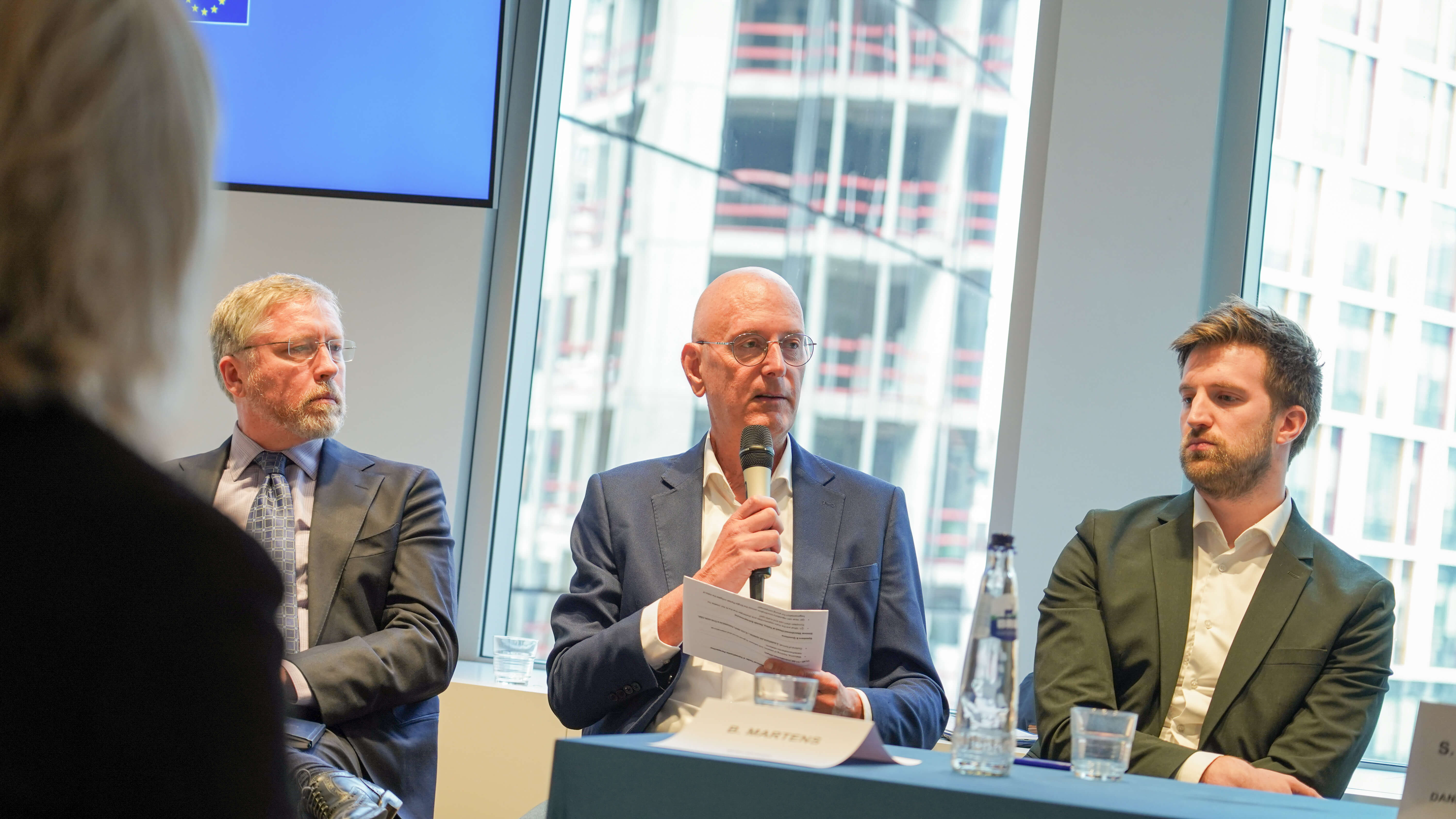 3 men in suits on a conference panel giving a presentation