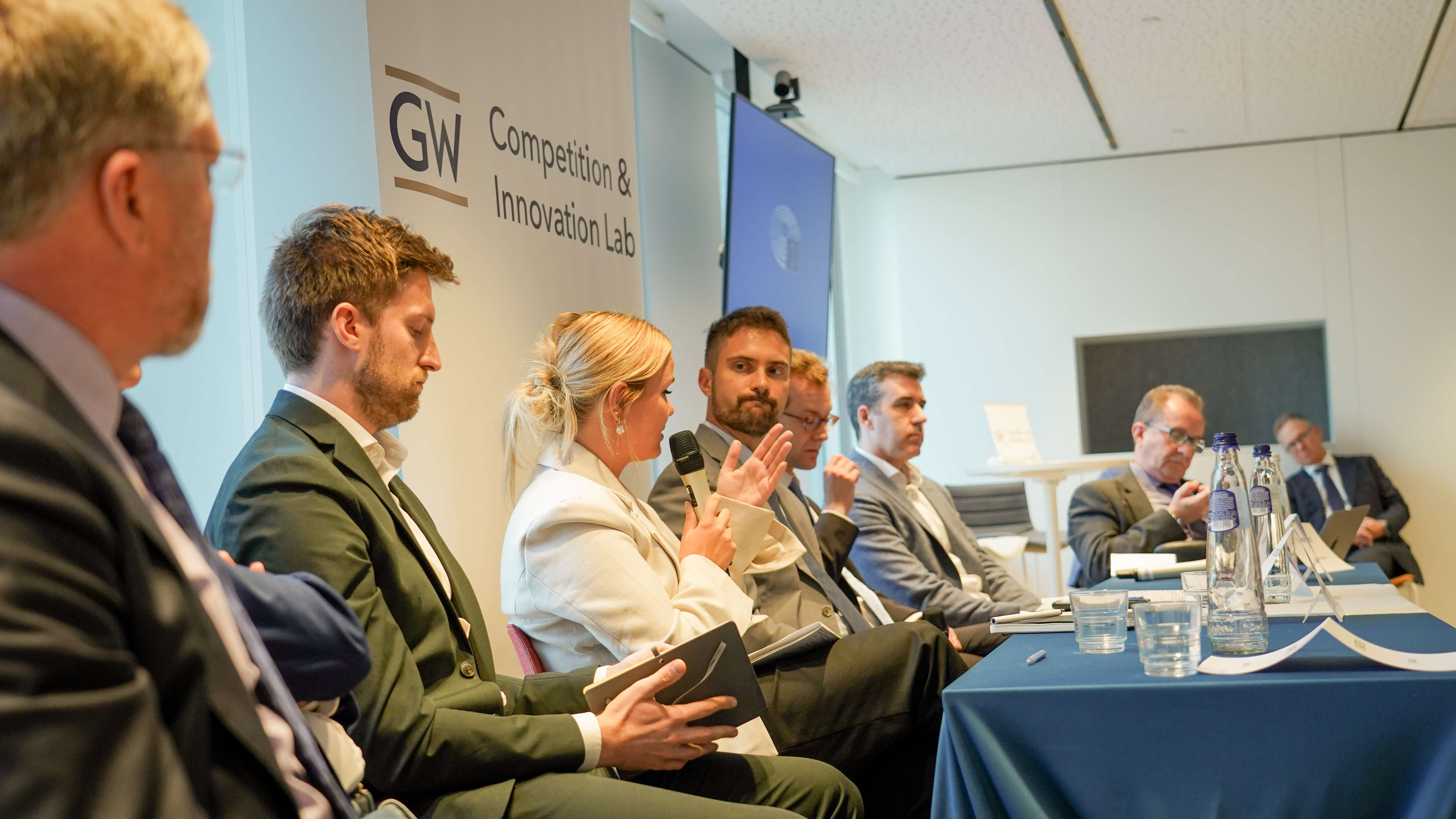 a conference panel of people in suits presenting to a crowd