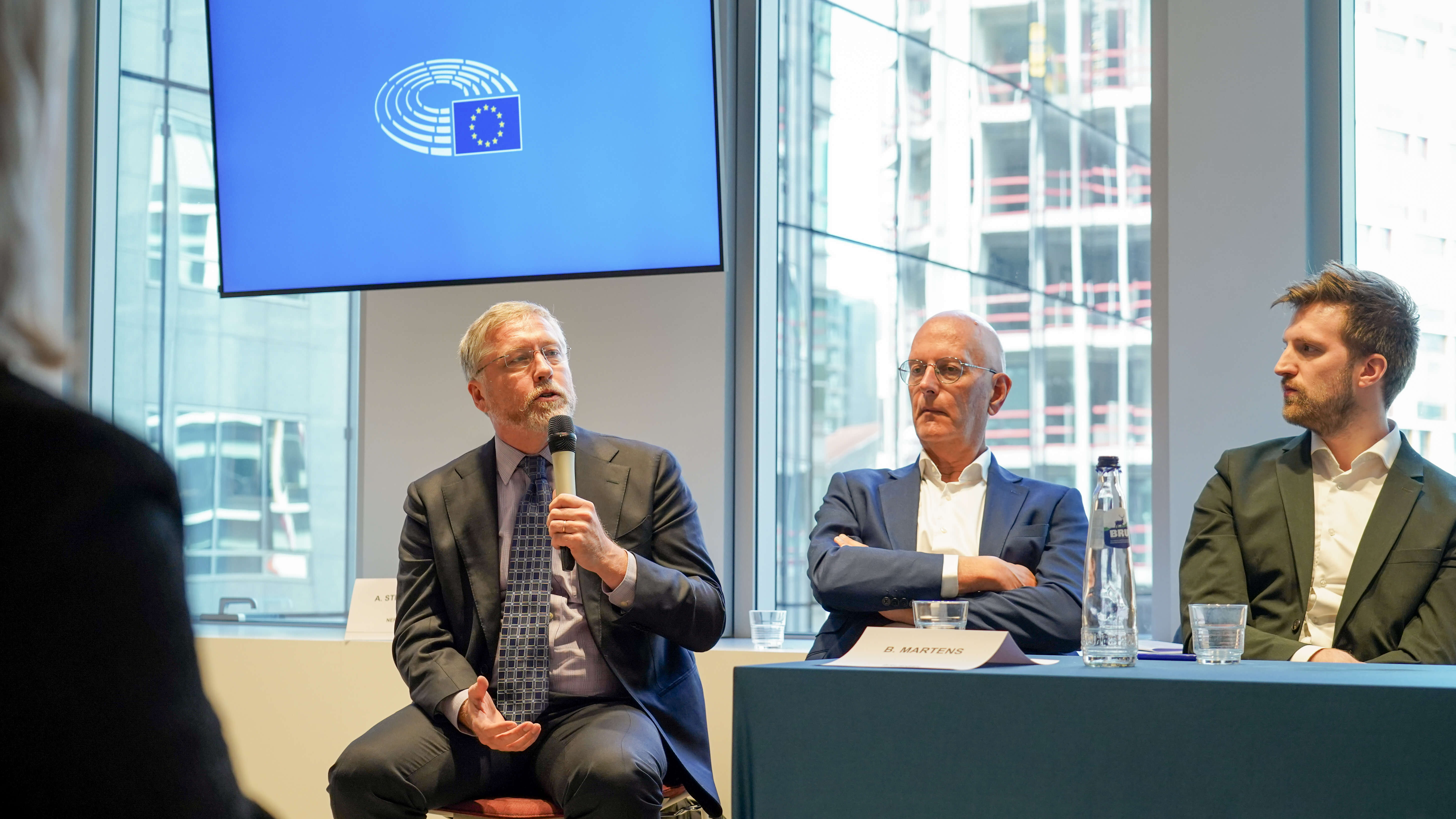 3 men in suits giving a conference presentation on a panel