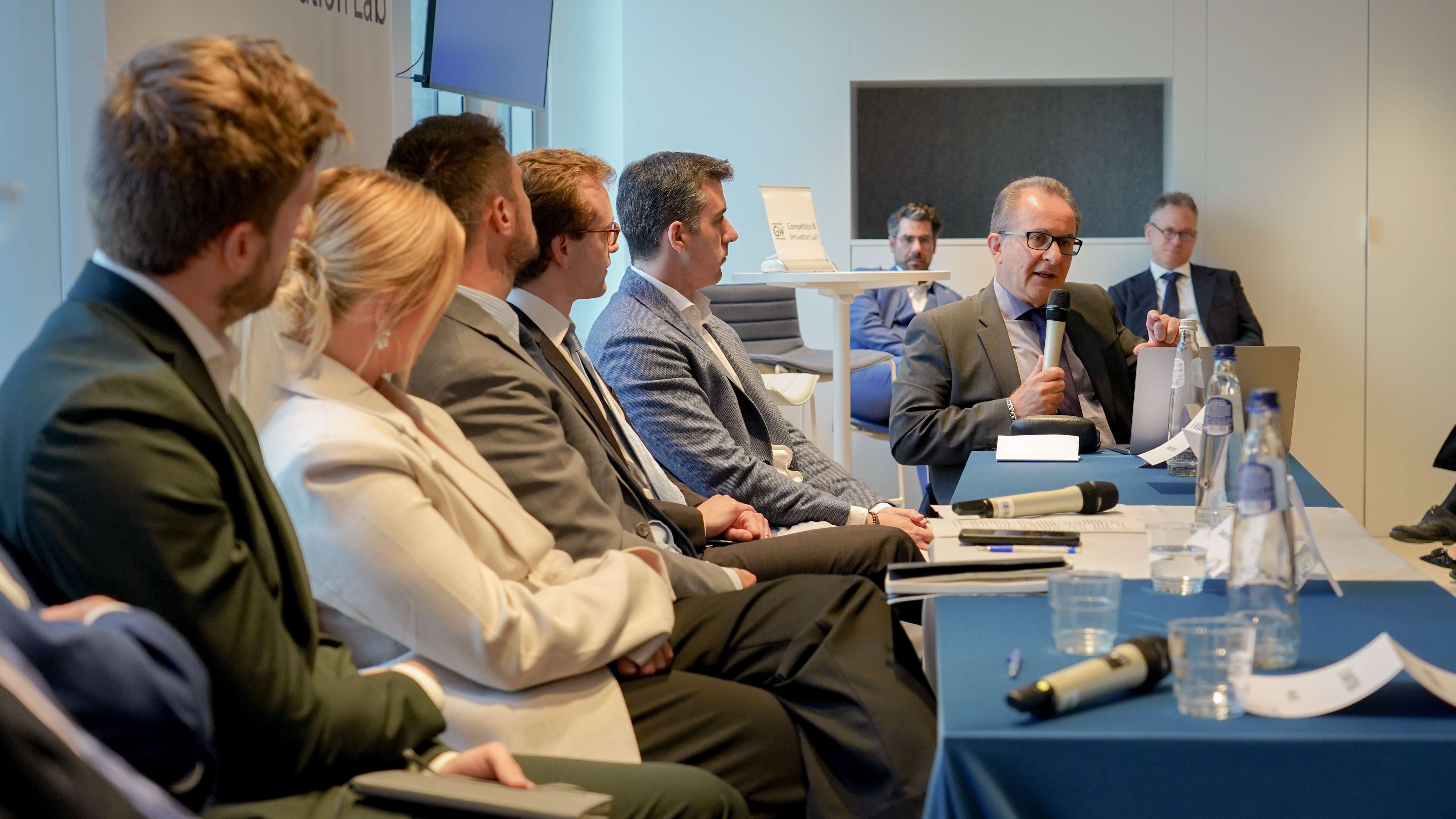 a conference panel of men and women in business wear giving a presentation