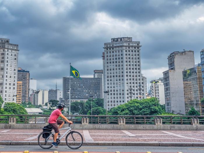 A man riding his bike in Sao Paolo with the city skyline visible behind him