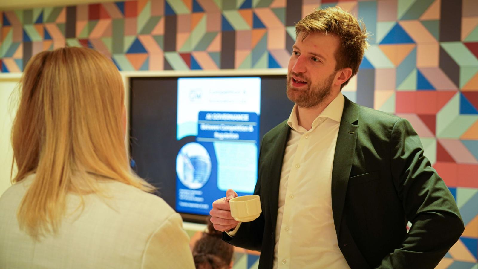 A man in a suit and woman in business wear having a casual conversation at a conference