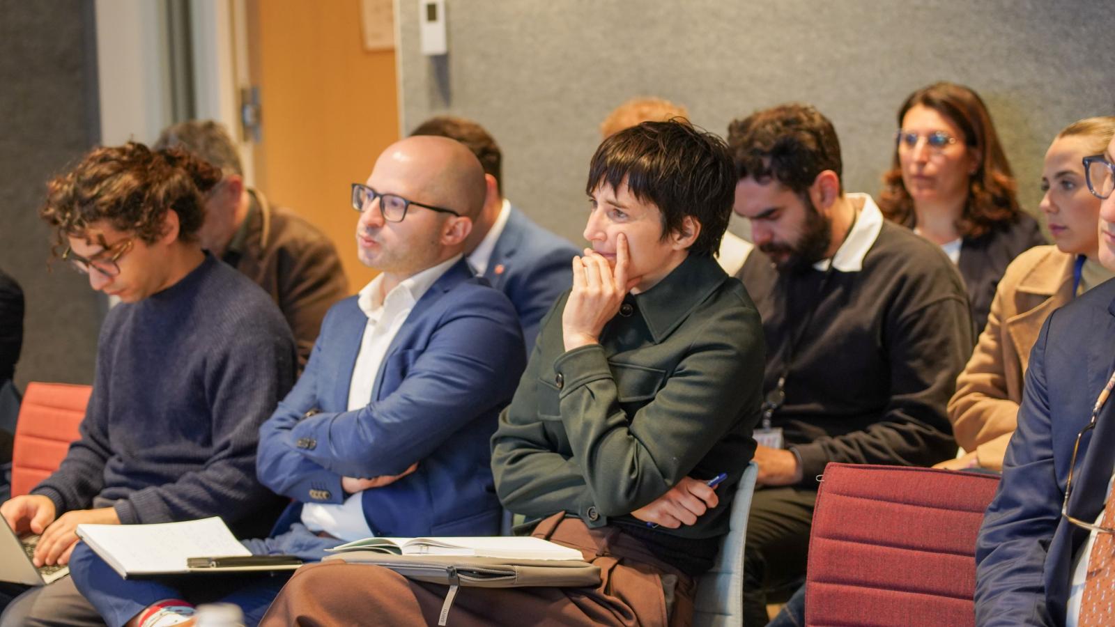 a crowd of people in business wear watches a conference presentation