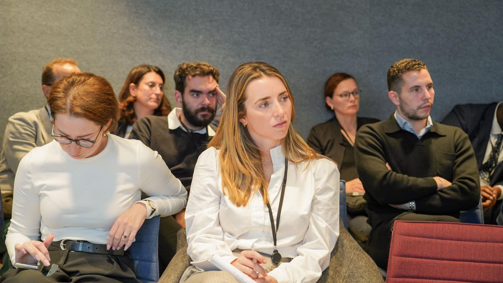 a crowd of people in business wear watches a conference presentation