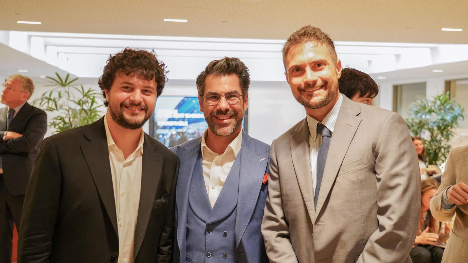 3 men in suits pose for a photo at a conference
