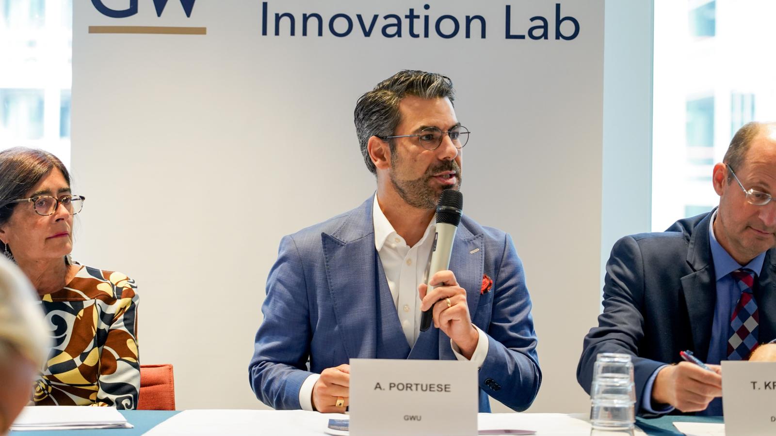 two men and a woman in business wear present at a conference in front of a GW sign