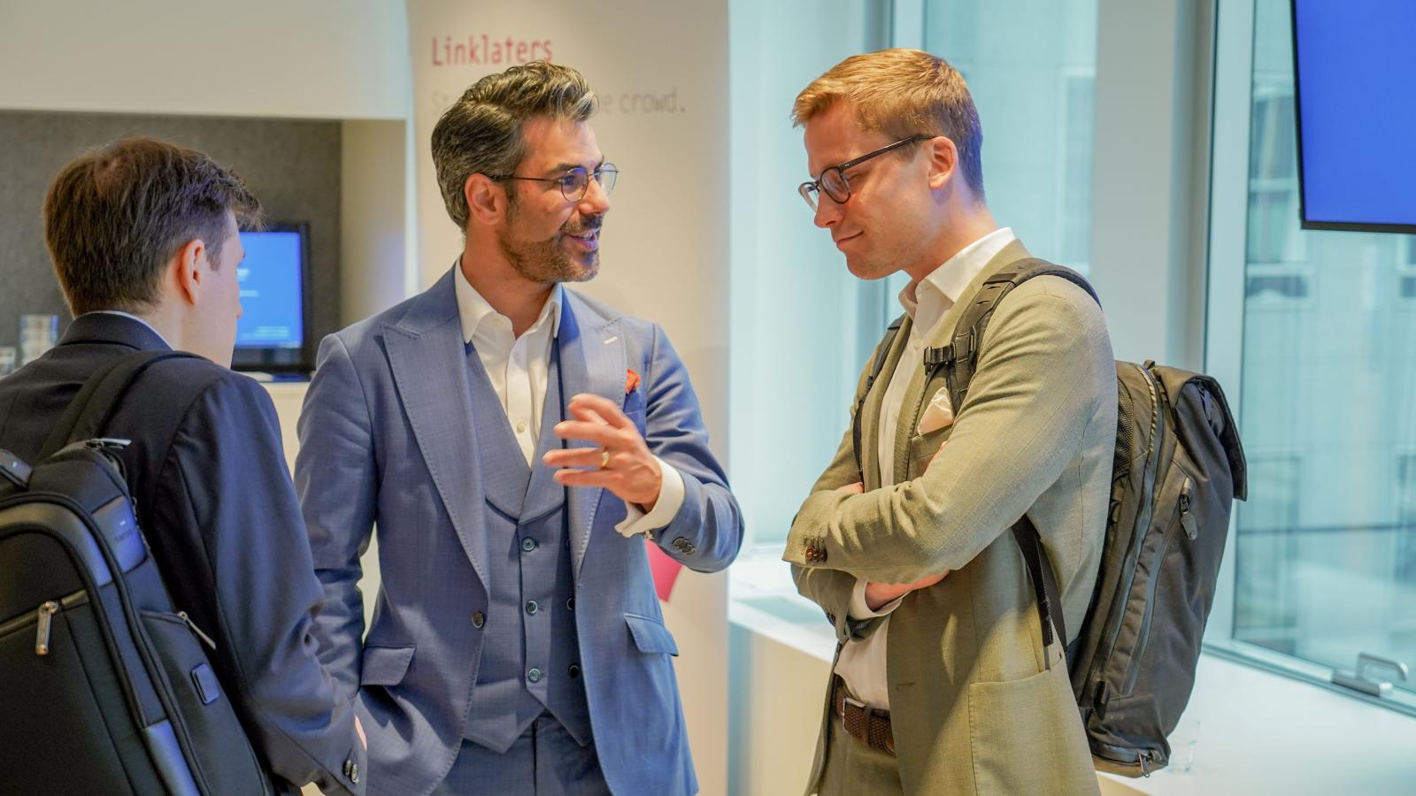 3 men in suits have a conversation at a conference